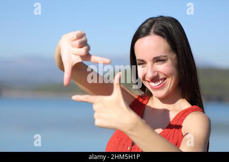 Donna felice in rosso inquadratura gesturing con le mani in un lago in vacanza Foto Stock