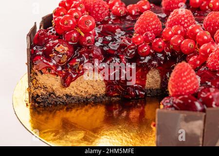 Primo piano di torta al cioccolato con aggiunta di gelatina di ciliegia e decorata con lamponi freschi e ribes rosso Foto Stock