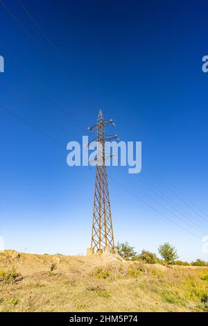 Il polo ad alta tensione o la torre elettrica è l'alimentazione ad alta tensione della trasmissione situata sul campo verde. Concetto di tecnologia energetica Foto Stock