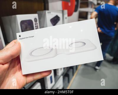 Parigi, Francia - Sep 24, 2021: POV mano maschio che tiene nuovi computer Apple Mag Safe Duo Charger per iPhone e Apple Guarda caricatore magnetico con i clienti sfocato in background - accessorio per caricare in modalità wireless l'iphone Foto Stock