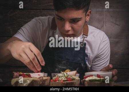 Bell'uomo giovane chef cucinare il pane in un tavolo di legno e sfondo di legno Foto Stock