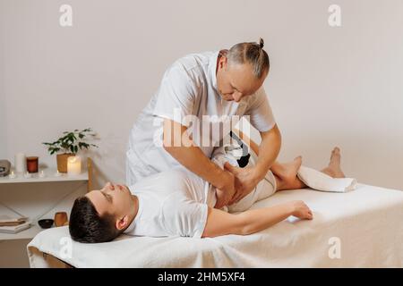 Massaggiatore forte e concentrato in uniforme che fa la terapia manuale per la schiena dell'atleta. Massaggio professionale e riabilitazione per sportivi. Concetto di benessere, corpo e assistenza sanitaria. Foto Stock