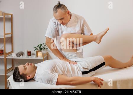 Massaggiatore forte e concentrato in uniforme che fa la terapia manuale per sportivo. Massaggio schiena professionale. Medicina alternativa. Concetto di benessere, corpo e assistenza sanitaria. Foto Stock