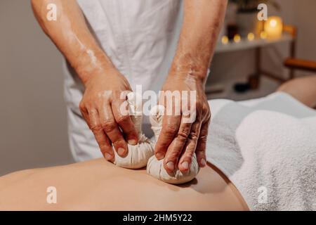 Primo piano schiena dell'uomo durante il tradizionale massaggio alle erbe tailandese. Medicina orientale con bustine aromatiche. Cura del corpo e SPA in Tailandia resort. Foto Stock