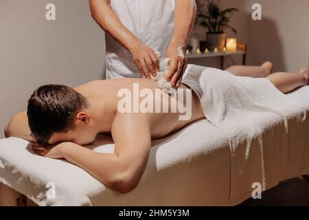 Uomo rilassante durante il tradizionale massaggio alle erbe thailandesi. Medicina orientale con bustine aromatiche. Cura del corpo e SPA in Tailandia resort. Foto Stock