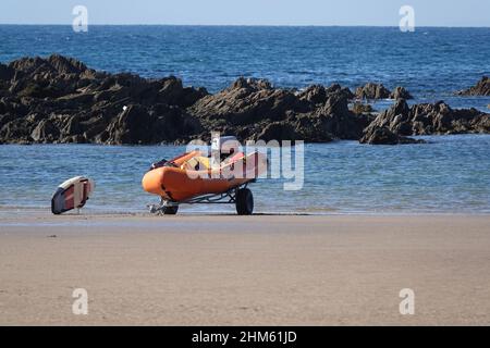 Una RIB RNLI o una barca gonfiabile rigida su un rimorchio su una spiaggia nel Regno Unito insieme ad una tavola di pagaia Foto Stock