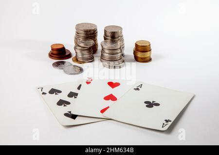 Tre carte da gioco e pile di monete giacciono su uno sfondo bianco. Foto Stock