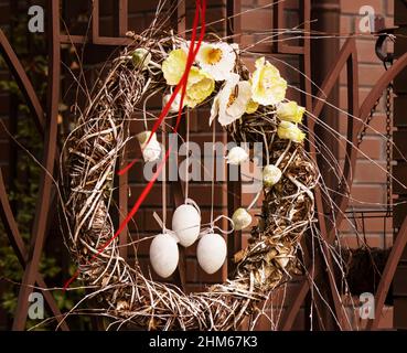 Tre uova di legno su nastri in una corona pasquale di rami di salice e fiori appesi alla porta. Benvenuto tradizionale corona pasquale decorata per E. Foto Stock