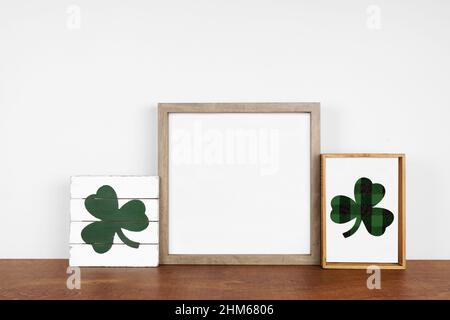 Mock up cornice in legno con St Patricks Day decor su una mensola in legno. Cartelli rustici in legno. Cornice quadrata contro una parete bianca. Spazio di copia. Foto Stock