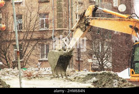 Dnepropetrovsk, Ucraina - 02.04.2022: Lavori di scavo in condizioni meteorologiche nevose. La benna dell'escavatore sposta il terreno scavato. Foto Stock