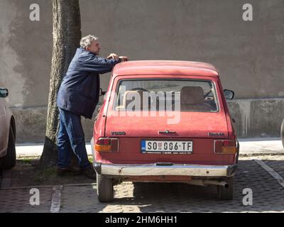 Foto di un'auto Skala, di colore rosso, con il marchio Zastava 55 e Yugo 55, parcheggiata in un parcheggio di Sombor Serbia con un vecchio uomo in piedi su di esso. Skala è Foto Stock