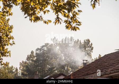 Foto del tetto di una casa residenziale con un fuoco sul suo camino, utilizzato per il riscaldamento, rejeting un po 'di fumi bianchi, in autunno. Foto Stock