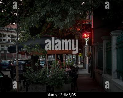 Foto della terrazza nel centro della città di Belgrado, Serbia, persone sedute in un caffè, la sera, con un cartello al neon che indica il bar, durante una somma Foto Stock