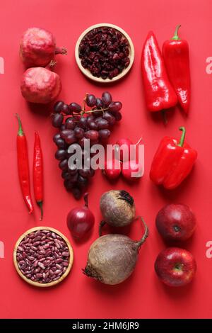 Frutta e verdura rossa su sfondo rosso. Melagrane, mirtilli secchi, paprika, peperoni cappy, ravanelli, uva, peperoni caldi, cipolla, barbabietole, a Foto Stock