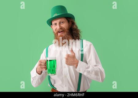 Uomo felice barbuto con un bicchiere di birra che mostra pollice su sfondo verde. Festa di San Patrizio Foto Stock