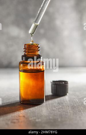 Una bottiglia di olio e una pipetta gocciolano olio cosmetico nella bottiglia. Vista frontale. Foto Stock