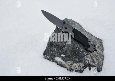 Il coltello pieghevole del campeggio si trova su una pietra in winter.Active attività di ricreazione escursioni e viaggi Foto Stock