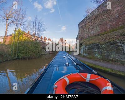 Vista da narrowboat viaggiando attraverso il paesaggio urbano inglese sul canale britannico con le mura della città vecchia Foto Stock