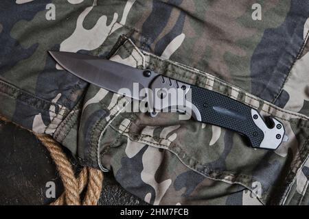 Coltello pieghevole tattico per la sopravvivenza e corda su abbigliamento militare camouflage Foto Stock