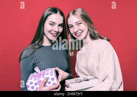 Due belle amiche hanno in mano dei regali e guardano la macchina fotografica con un sorriso. Le ragazze adorabili si donano a vicenda i regali. Amici. Nuovo sì Foto Stock