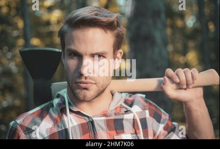 Lumberjack uomo porta l'ascia sulla spalla. Taglialegna con ascia nella foresta estiva. Lumberjack che tiene l'ascia. Foto Stock