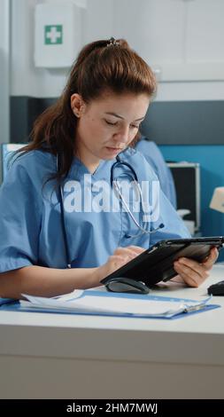 Assistente medico che digita sullo schermo del tablet e controlla il computer per l'appuntamento in ufficio medico. Infermiera che guarda il monitor mentre usa il gadget moderno per visita di controllo sanitario. Foto Stock