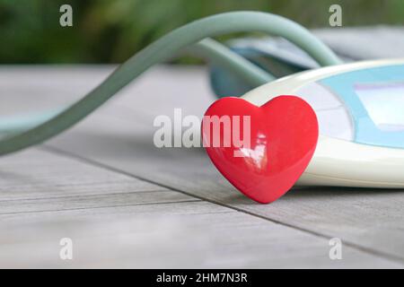 Forma del cuore di colore rosso accanto al manometro digitale della pressione sanguigna. Salute e concetto medico. Foto Stock