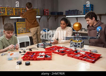 Gruppo diversificato di bambini adolescenti che costruisce robot in classe ingegneristica a scuola moderna, spazio copia Foto Stock