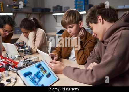 Un gruppo diversificato di bambini che utilizza tablet digitali mentre programmano robot in classe ingegneristica presso la scuola moderna Foto Stock