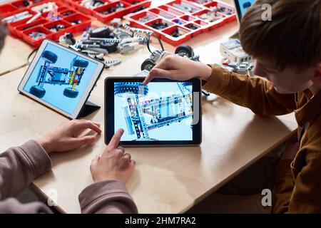 Primo piano di due bambini che usano il tablet digitale mentre programmano il robot in classe ingegneristica presso la scuola moderna, spazio copia Foto Stock