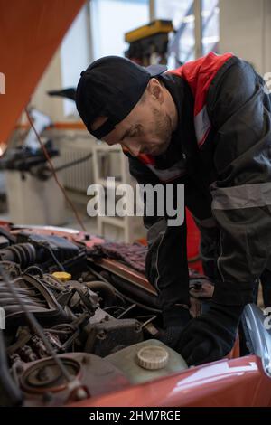 Ritratto verticale del meccanico maschile che guarda sotto il cofano mentre ripara l'auto nel negozio di auto Foto Stock