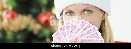 Ritratto di giovane bella donna in babbo natale cappello tenendo carte da gioco sullo sfondo di albero di Capodanno Foto Stock