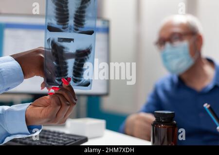Primo piano del medico mano di mano di tenuta dei polmoni radiografia di discussione di esperienza medica con l'uomo anziano in pensione durante l'esame della malattia nell'ufficio dell'ospedale. Concetto di medicina durante il coronavirus Foto Stock