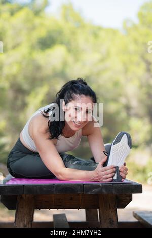 Felice donna caucasica adulta che allunga la gamba su un tavolo da picnic nel parco Foto Stock