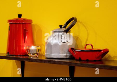 Cucina interna con stoviglie, piatti, teglia in ferro e teiera su una mensola contro il muro giallo Foto Stock