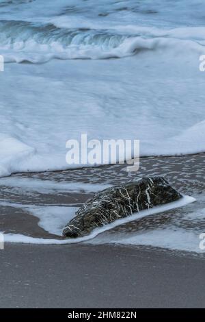 Marea entrante che scorre intorno ad una roccia su una spiaggia. Foto Stock