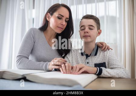 Donna aiuta il ragazzo cieco a leggere un libro in braille. Foto Stock