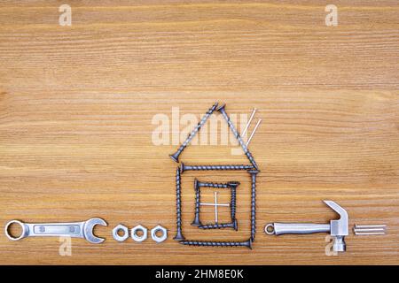 Profilo della casa fatto da viti e chiodi con utensili a mano e dadi disposti su un fondo di legno. Kit di manutenzione per uso domestico. Foto Stock