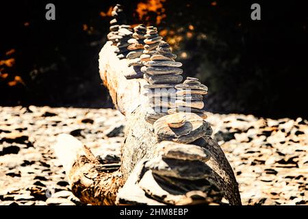 Pietre impilate su un vecchio tronco di albero in un letto di roccia del fiume durante l'autunno Foto Stock