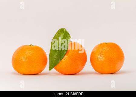 Tre agrumi di mandarino arancio, uno con foglia verde, isolato su sfondo bianco Foto Stock