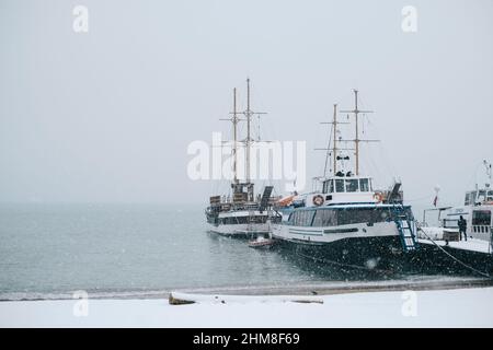 Gelendzhik, Russia, 24 gennaio 2022: Barche marine vicino al molo durante una nevicata in inverno. Foto Stock