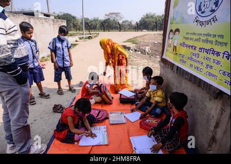 Nabin Nagar, Bengala Occidentale, India. 7th Feb 2022. Il governo dello Stato del Bengala occidentale ha lanciato "'˜Paray Shikshalaya' a decorrere dal 7th febbraio, Uno sforzo di scolarizzazione basato sulla comunità nei quartieri che mira gli studenti primari a mirare al programma è quello di svezzare una grande sezione di studenti che ha abbandonato il sistema di istruzione formale negli ultimi due anni a causa della chiusura delle scuole, a causa di Covid-19. Una classe preprimaria della scuola elementare di confine India-Bangladesh è stata portata su una strada vuota accanto alla recinzione a Nabin Nagar, ci sono occasionalmente animali domestici che entrano. (Credito Foto Stock