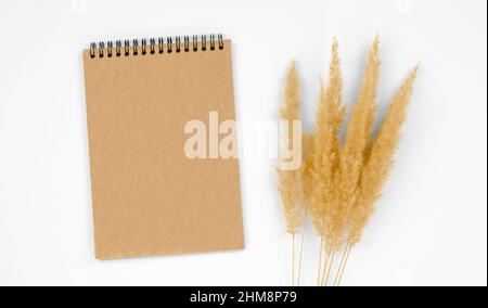 Blocco note vuoto con carta kraft su sfondo bianco con pampas erba. Modulo per congratulazioni o inviti. Foto Stock