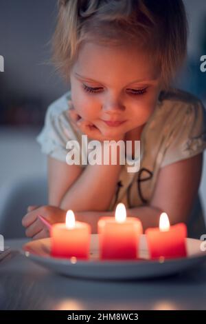 Primo piano della candela illuminata Girl Holding. Carino ragazza piccola sopra tre candele rosse. Piccolo bambino che guarda le luci di candela. Foto Stock