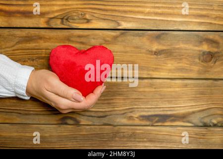 Primo piano del cuore rosso giocattolo nel palmo di una donna. Vecchio sfondo di legno grunge. Spazio per il testo. Profondità di campo poco profonda. Foto Stock