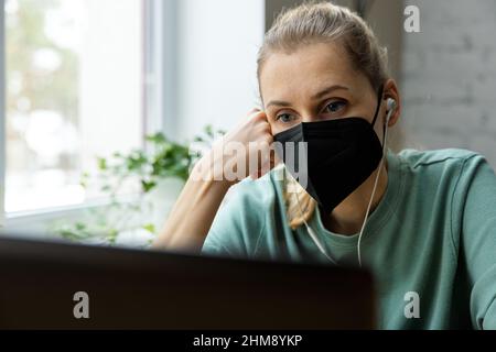 Donna con maschera facciale FFP2 che lavora con il computer in ufficio. Sicurezza sul posto di lavoro Foto Stock