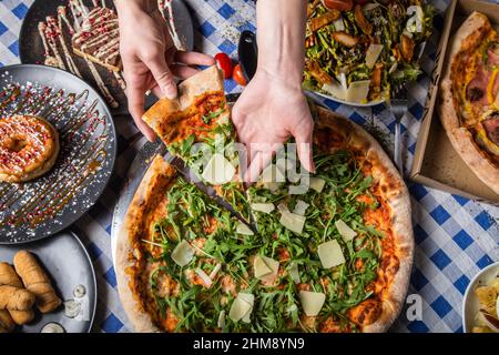 Le mani della donna ospite prendono una fetta di pizza al tavolo del ristorante Foto Stock