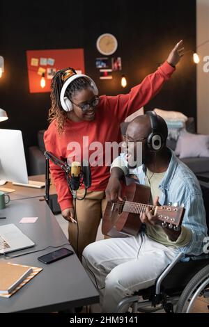 Felice uomo africano con disabilità suonare la chitarra e cantare una canzone insieme alla donna durante la trasmissione dal vivo Foto Stock