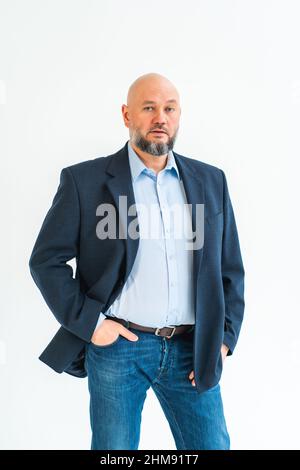 Foto verticale dell'uomo maturo che rimane su sfondo bianco in studio. Guardando seriamente nella fotocamera. Indossare jeans, giacca Foto Stock