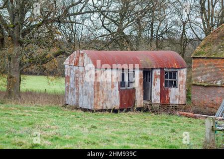Un disuso e dilapidato, arrugginito, capannone di ferro in un campo a Vann, vicino Ockley, Surrey Foto Stock